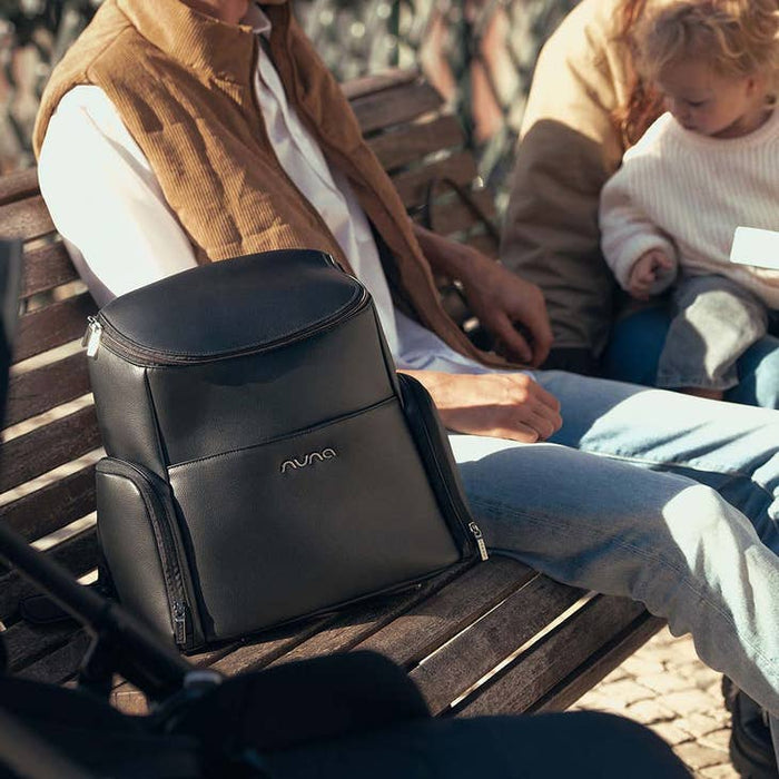[Espresso]  Black backpack with 'Nuvola' branding on a wooden bench, people sitting in the background.