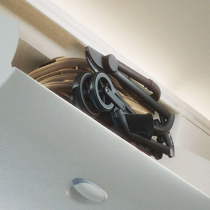 Compactly folded travel stroller stowed in an airplane overhead bin.