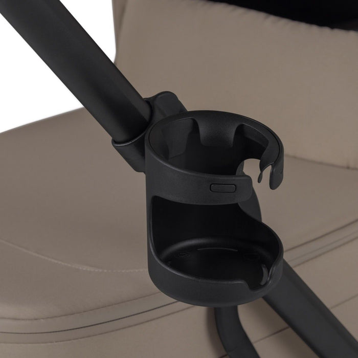 Black cup holder attached to the frame of a beige stroller.